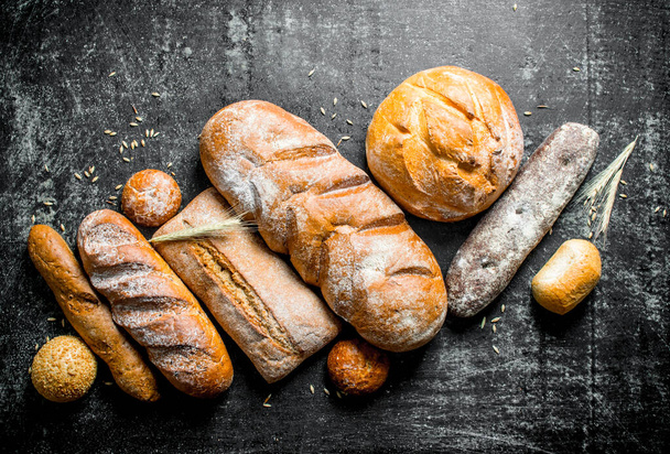 A variety of fresh baked bread. On dark rustic background - Foto, immagini