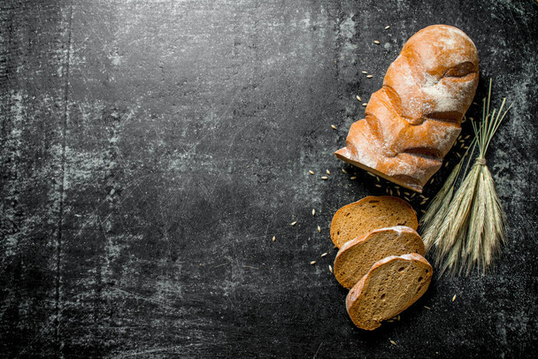 Pieces of rye bread with spikelets. On black rustic background - 写真・画像