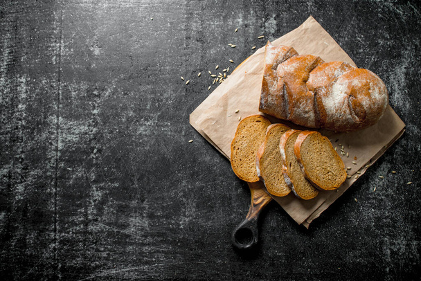 Gesneden brood op een snijplank met papier. Op donkere rustieke achtergrond - Foto, afbeelding