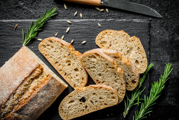 Pieces of bread ciabatta with rosemary. On black rustic background - Zdjęcie, obraz