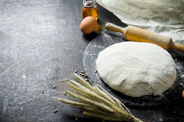 Fresh dough with spikelets and a rolling pin. On dark rustic background - Foto, Imagem