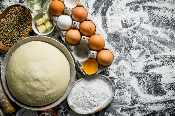 Dough with eggs, butter and grain in bowls. On rustic background - Photo, Image