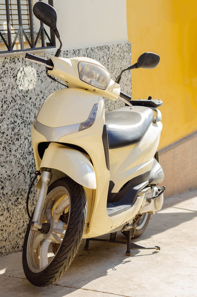 A scooter parked on a narrow Spanish street by the side of a building, a city vehicle - Zdjęcie, obraz