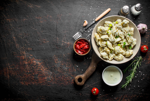 Dumplings with spices, garlic, sour cream and tomato paste. On dark rustic background - 写真・画像