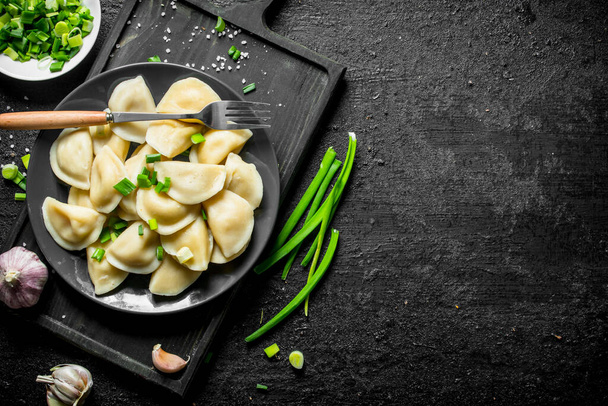 Dumplings on a plate with green onions and garlic. On black rustic background - Φωτογραφία, εικόνα