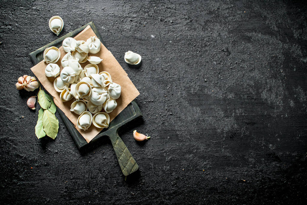 Homemade raw dumpling with garlic cloves and Bay leaf. On black rustic background - Photo, Image