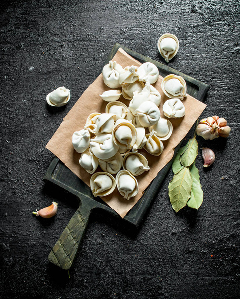Homemade raw dumpling with garlic cloves and Bay leaf. On black rustic background - 写真・画像