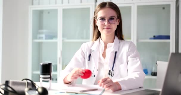Női orvos tartja piros játék szív kezében közelkép. Belső szervek átültetése - Felvétel, videó