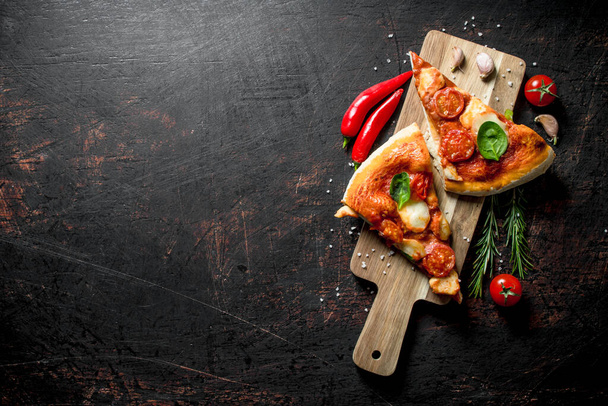 Slices of homemade pizza on a cutting Board with chili, tomatoes and rosemary. On rustic background - Фото, изображение
