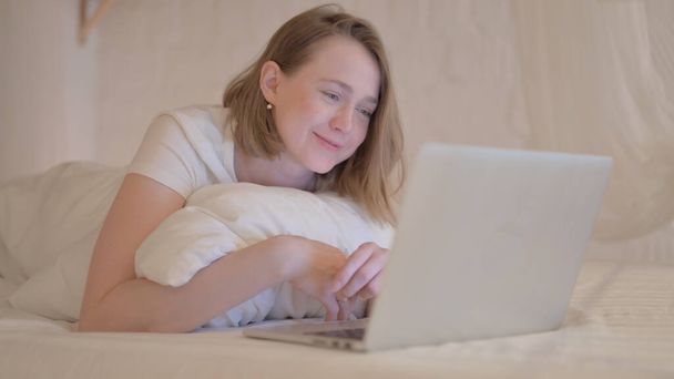 Онлайн видео чат молодой женщины на ноутбуке во время лежания на животе в постели - Фото, изображение