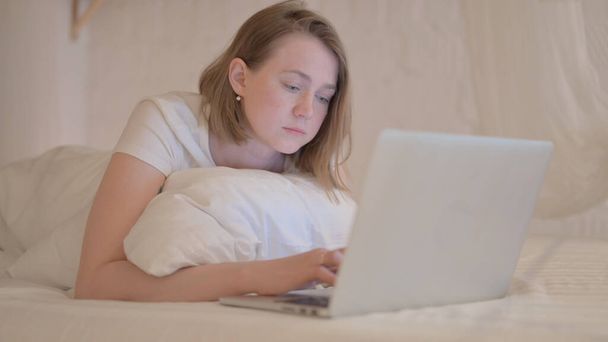 Jeune femme travaillant sur ordinateur portable tout en s'allongeant sur l'estomac au lit - Photo, image