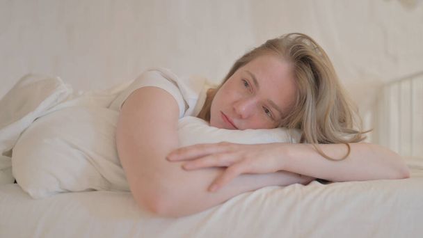 Pensive nuori nainen makaa sängyssä, kun makaa vatsa - Valokuva, kuva