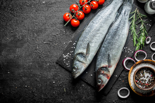 Raw fish with spices, cherry tomatoes and chopped onions. On black rustic background - Foto, Imagem