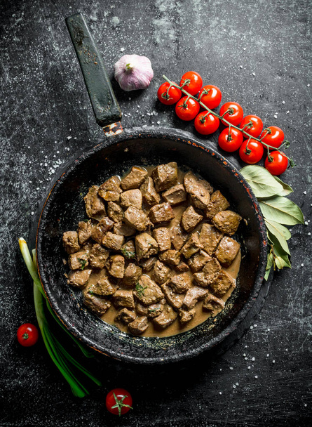 Fried pieces of liver with garlic, cherry tomatoes and Bay leaf. On dark rustic background - Φωτογραφία, εικόνα