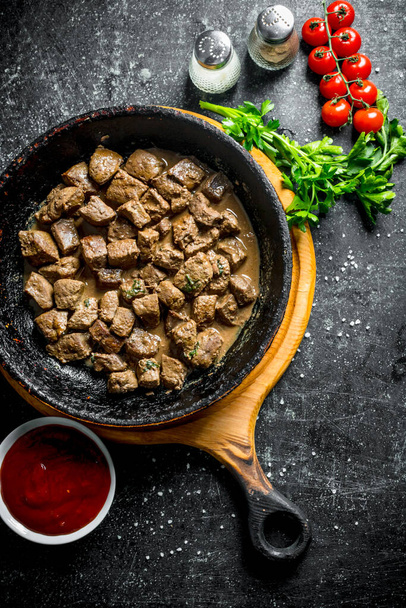 Pieces of cooked liver with sauce, parsley and tomatoes. On dark rustic background - Foto, afbeelding