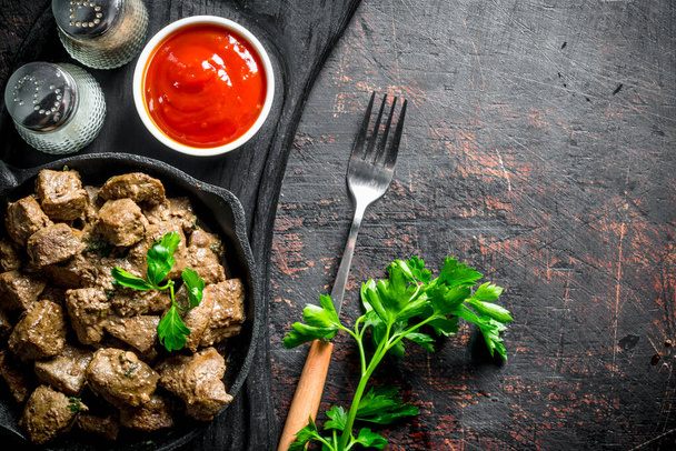 Fried liver in a frying pan on a cutting Board with parsley, sauce and spices. On dark rustic background - Foto, Imagem