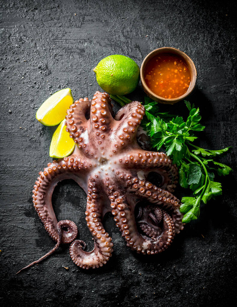 Fresh octopus with parsley, lime and sauce in bowl. On black rustic background - Zdjęcie, obraz