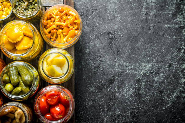 Jars with variations of pickled food on a tray. On dark rustic background - Photo, image