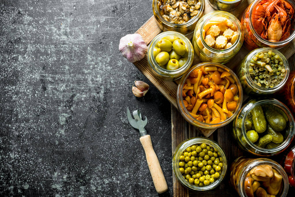 Jars with variations of pickled food on a tray. On dark rustic background - Foto, afbeelding