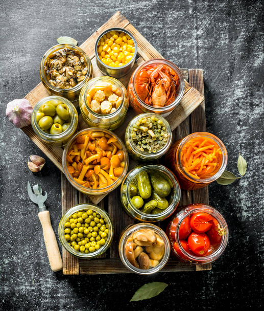 Different preserved food on a wooden tray. On dark rustic background - Foto, Imagem