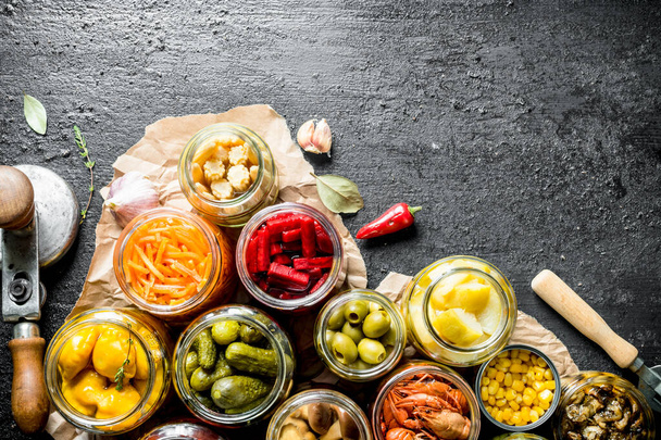 Assortment of different preserved food in glass jars on paper. On black rustic background - Photo, Image