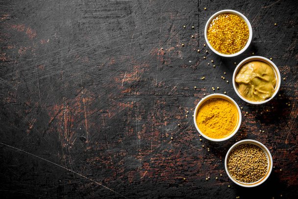 Different kinds of mustard in the bowls. On dark rustic background - Fotoğraf, Görsel