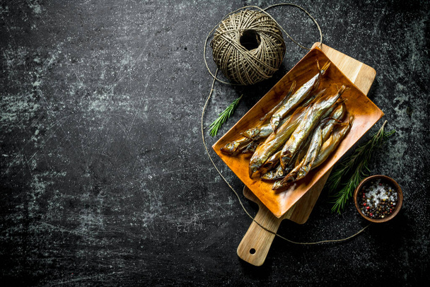 Smoked fish on a cutting Board with spices and twine. On dark rustic background - Foto, imagen