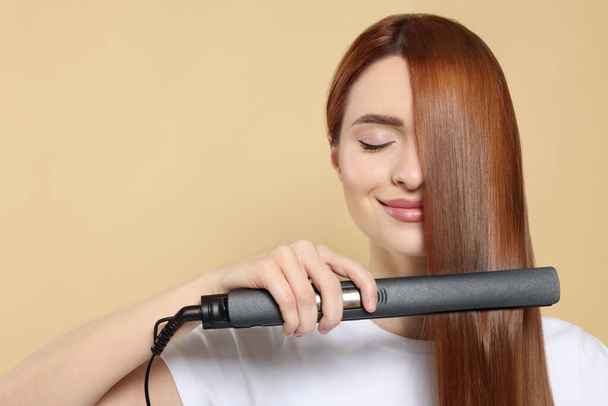 Beautiful woman using hair iron on beige background, space for text - Foto, Imagen