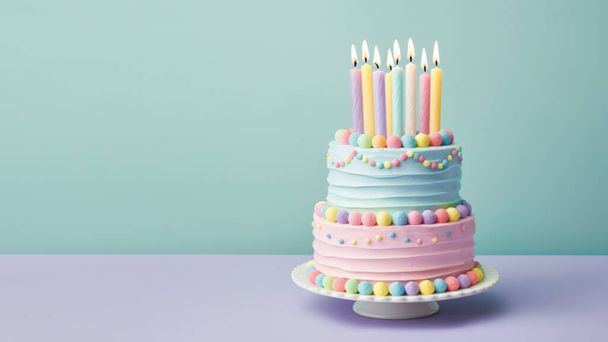 Pastel colored tiered birthday cake decorated with candies and colorful candles with pastel buttercream frosting against a plain turquoise background - Photo, image