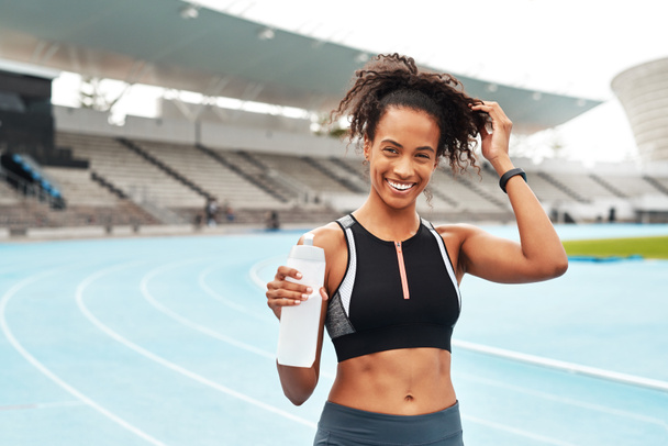 Fitness, running and portrait of happy woman with water at stadium, relax at marathon training or exercise. Workout, health and body, female sports runner at arena track with smile and bottle - Fotó, kép