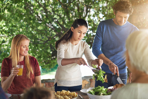 Nourriture, salade et aide avec la famille au déjeuner dans la nature pour la santé, le collage et la célébration. Vacances, barbecue et événement avec parents et enfants qui mangent ensemble pour le jardin, les générations et le bien-être. - Photo, image