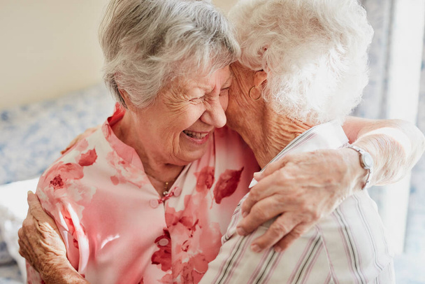 Happy, hug and senior woman friends laughing in the bedroom of a retirement home together. Smile, reunion and laughter with an elderly female pensioner and friend bonding indoor during a visit. - Foto, afbeelding