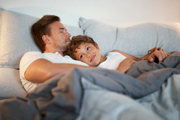 Looks like dad had a long day. a man and his son lying in a bed together - Fotoğraf, Görsel