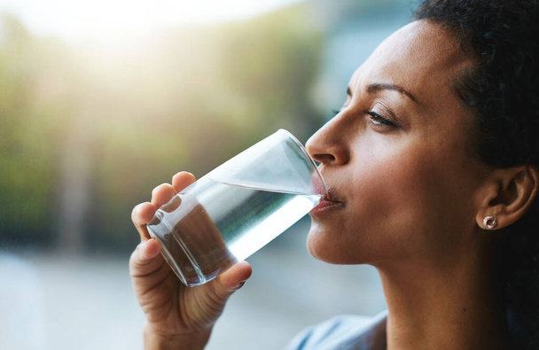 Health, glass and woman drinking water, wellness and nutrition at home, happiness and refreshment. Female person, happy and lady with clear liquid, natural and care with a smile, fresh and hydration. - Photo, Image