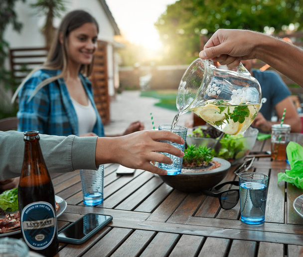 Its a gathering of friends. two unrecognizable friends pouring water in a glass for each other outside around a table in a garden - Foto, Imagem