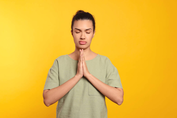 Afroameričanka se sepjatýma rukama modlí k Bohu na oranžovém pozadí - Fotografie, Obrázek