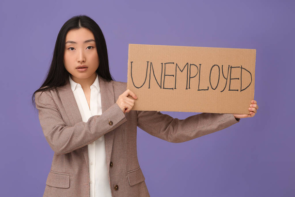 Asian woman holding sign with word Unemployed on purple background - 写真・画像