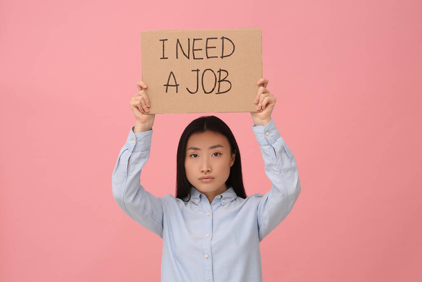 Unemployed Asian woman holding sign with phrase I Need A Job on pink background - Foto, Imagen