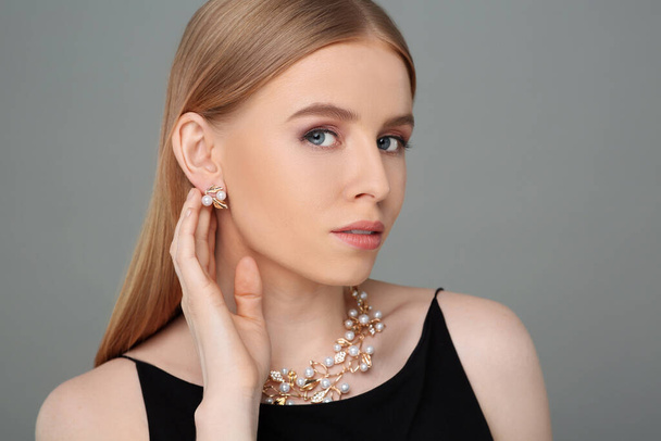 Beautiful young woman with elegant jewelry on gray background - Fotó, kép