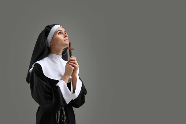 Nonne mit Kreuz betet zu Gott auf grauem Hintergrund. Raum für Text - Foto, Bild