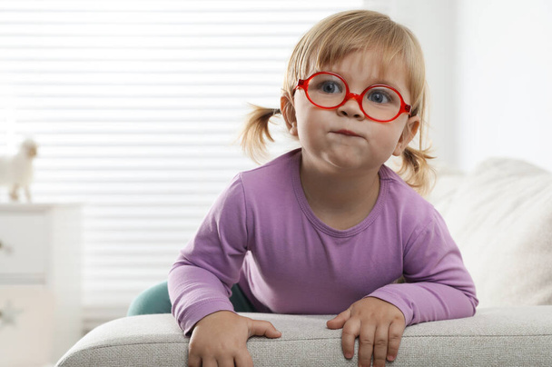 Cute little girl in glasses on sofa at home. Space for text - Foto, imagen