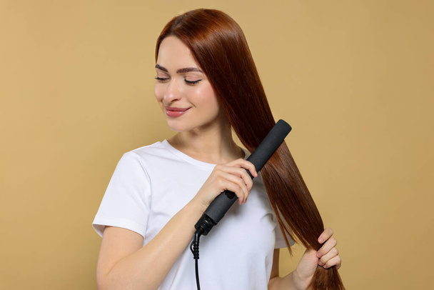 Beautiful woman using hair iron on beige background - Zdjęcie, obraz