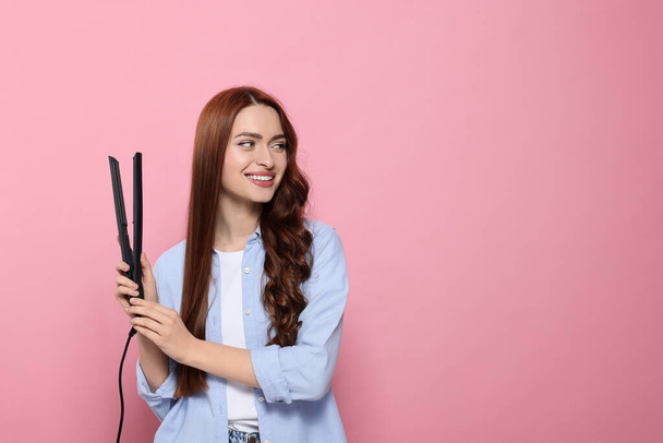 Beautiful woman with hair iron on pink background, space for text - Fotografie, Obrázek