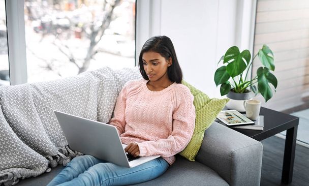 Woman, laptop and typing on home sofa for student research, streaming or social media. Indian female person on a couch to relax, surfing internet or writing email for communication on website. - Φωτογραφία, εικόνα
