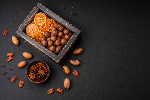 Pecanas asadas y nueces de macadamia, mandarina seca, bayas secas sobre un fondo de hormigón oscuro - Foto, imagen
