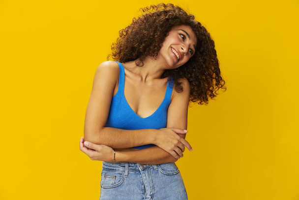 Femme avec des cheveux afro frisés dans un t-shirt bleu. signes de fond jaune avec ses mains, regarder dans l'appareil photo, sourire avec les dents et le bonheur, copier l'espace. Photo de haute qualité - Photo, image