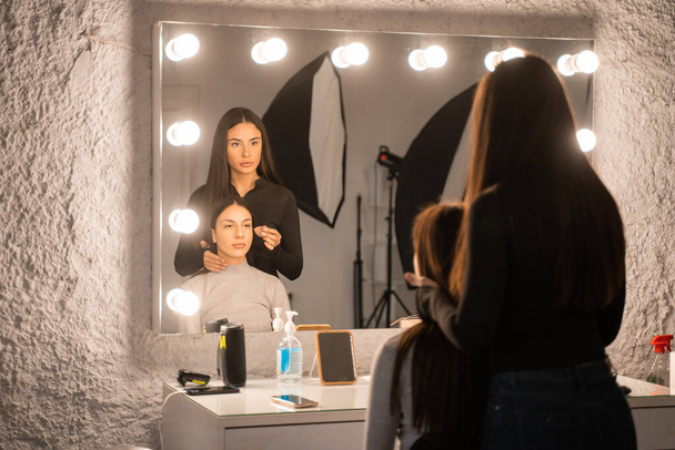 Stylist woman making make up for client girl. Young lady professional applying visage at brunette woman face. Occupation concept - Photo, Image
