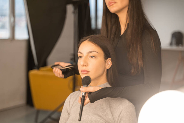 Brunette girl enjoying makeup and styling in salon. Cropped view of the make-up artist making visage. Personal care and beauty salon concept - Foto, Imagem
