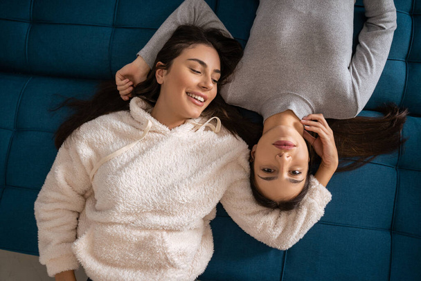 Top view of the happy women relaxing on blue sofa and bonding to each other at home. Young girls relaxing on couch in apartment - Valokuva, kuva