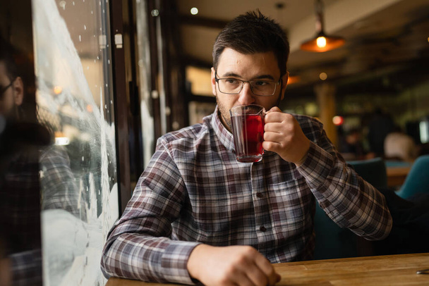 Ένας ενήλικας καυκάσιος που κάθεται μόνος του στο καφέ μπροστά από ένα αρσενικό με γένια και γυαλιά κρατώντας ένα φλιτζάνι τσάι οι πραγματικοί άνθρωποι αντιγράφουν το χώρο - Φωτογραφία, εικόνα